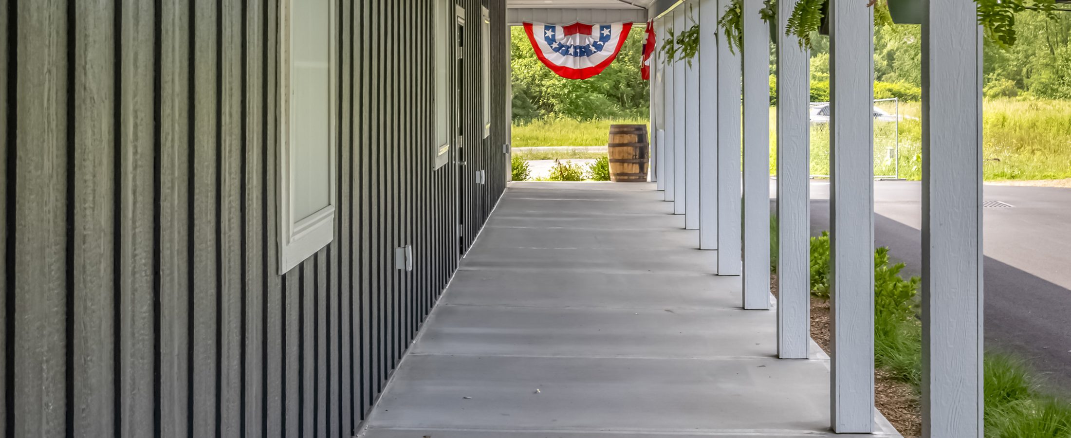The covered walkway along the Farmers Choice New Paltz barn, hanging ferns and open fields beyond